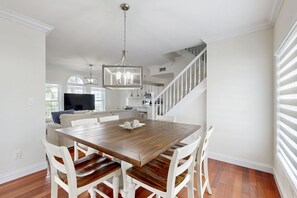 A dining area with a wooden table and white chairs, a chandelier, and a staircase leading to an upper level. - Waterfront home w/hot tub, gas grill, WiFi, AC, near attractions (Key Largo)