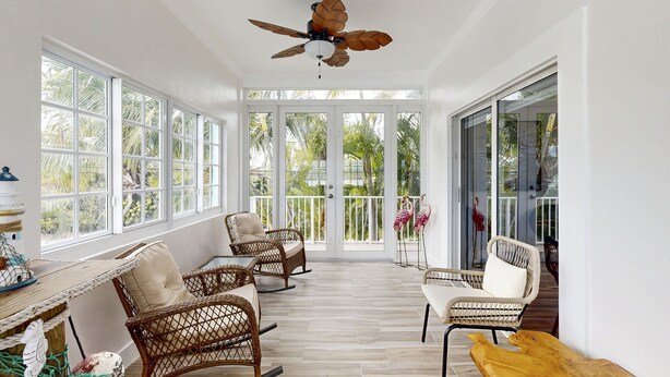 A spacious room with large windows, wicker furniture, and a ceiling fan. - Waterfront home w/hot tub, gas grill, WiFi, AC, near attractions (Key Largo)