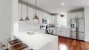 A modern kitchen with white cabinetry, stainless steel appliances, and a central island with stools. - Waterfront home w/hot tub, gas grill, WiFi, AC, near attractions (Key Largo)