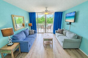 A living room with two sofas, a coffee table, a TV, and a ceiling fan. - Sunrise Suites Condo with Balcony - Shared Pool, Hot Tub, Tennis, Free Parking (Key West)