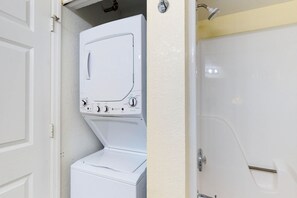 Ein kleiner Waschraum mit einer Waschmaschine und einem Trockner, einer Dusche und einer Tür zu einem weiteren Raum.
