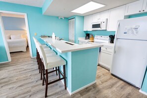 A modern kitchen with a central island, white cabinetry, and a wooden floor. - Sunrise Suites Condo with Balcony - Shared Pool, Hot Tub, Tennis, Free Parking (Key West)