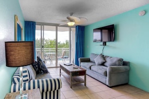 A living room with a sofa, a coffee table, a television, and a ceiling fan. - Sunrise Suites Condo with Balcony - Shared Pool, Hot Tub, Tennis, Free Parking (Key West)
