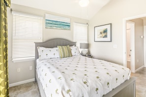 A bedroom with a bed, two windows with blinds, a nightstand, a lamp, and a wall with two framed pictures. - Immaculate oceanfront townhouse with ocean view & private beach access (Duck Key)