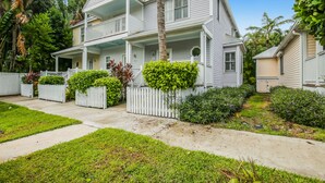 A two-story house with a porch, surrounded by a white picket fence and lush greenery. - Tropical oasis near all the action with central AC & balcony (Duck Key)