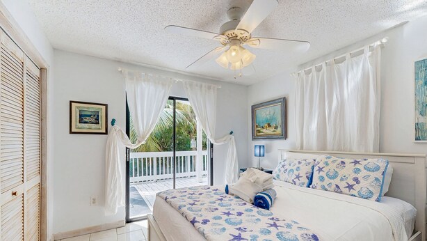 A bedroom with a bed, a ceiling fan, and a view of the outside. - Dog friendly Florida Keys Home with Grill, Patio & Fully Equipped Kitchen (Key Largo)