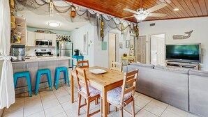 A cozy kitchen with wooden cabinets, a microwave, and a dining area with a wooden table and blue stools. - Dog friendly Florida Keys Home with Grill, Patio & Fully Equipped Kitchen (Key Largo)