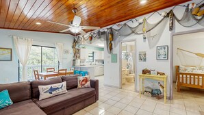 A cozy living room with a brown sofa, a dining area, and a kitchen in the background. - Dog friendly Florida Keys Home with Grill, Patio & Fully Equipped Kitchen (Key Largo)