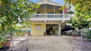 A two-story building with a covered balcony, a boat parked outside, and a sign reading "Beach House." - Dog friendly Florida Keys Home with Grill, Patio & Fully Equipped Kitchen (Key Largo)