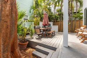 Une terrasse en bois avec des meubles d’extérieur, une plante en pot et un escalier menant à une zone abritée.