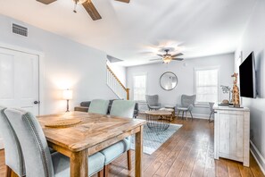 Un salon spacieux avec une table à manger en bois, des sièges confortables, un ventilateur de plafond et un escalier menant à un autre niveau.