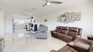 Uma sala de estar moderna com um sofá de couro marrom, uma poltrona cinza e um ventilador de teto.