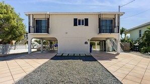 Um edifício de dois andares com entrada central, uma área coberta com um banco e uma escadaria que leva a um andar superior.