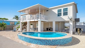 Ein zweistöckiges Haus mit Swimmingpool, überdachter Terrasse und einer Holzterrasse.