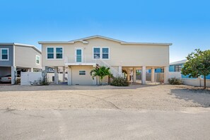 A two-story building with a covered parking area, a staircase, and a small garden with palm trees. - Canal-front Dog-Friendly Home with private pool, WiFi, washer/dryer & central AC (Marathon)