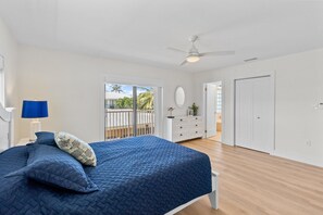 A bedroom with a bed, a ceiling fan, a dresser, and a door. - Waterfront duplex with hot tub, pool, & beach access - W/D, balcony, and grill (Key Colony Beach)