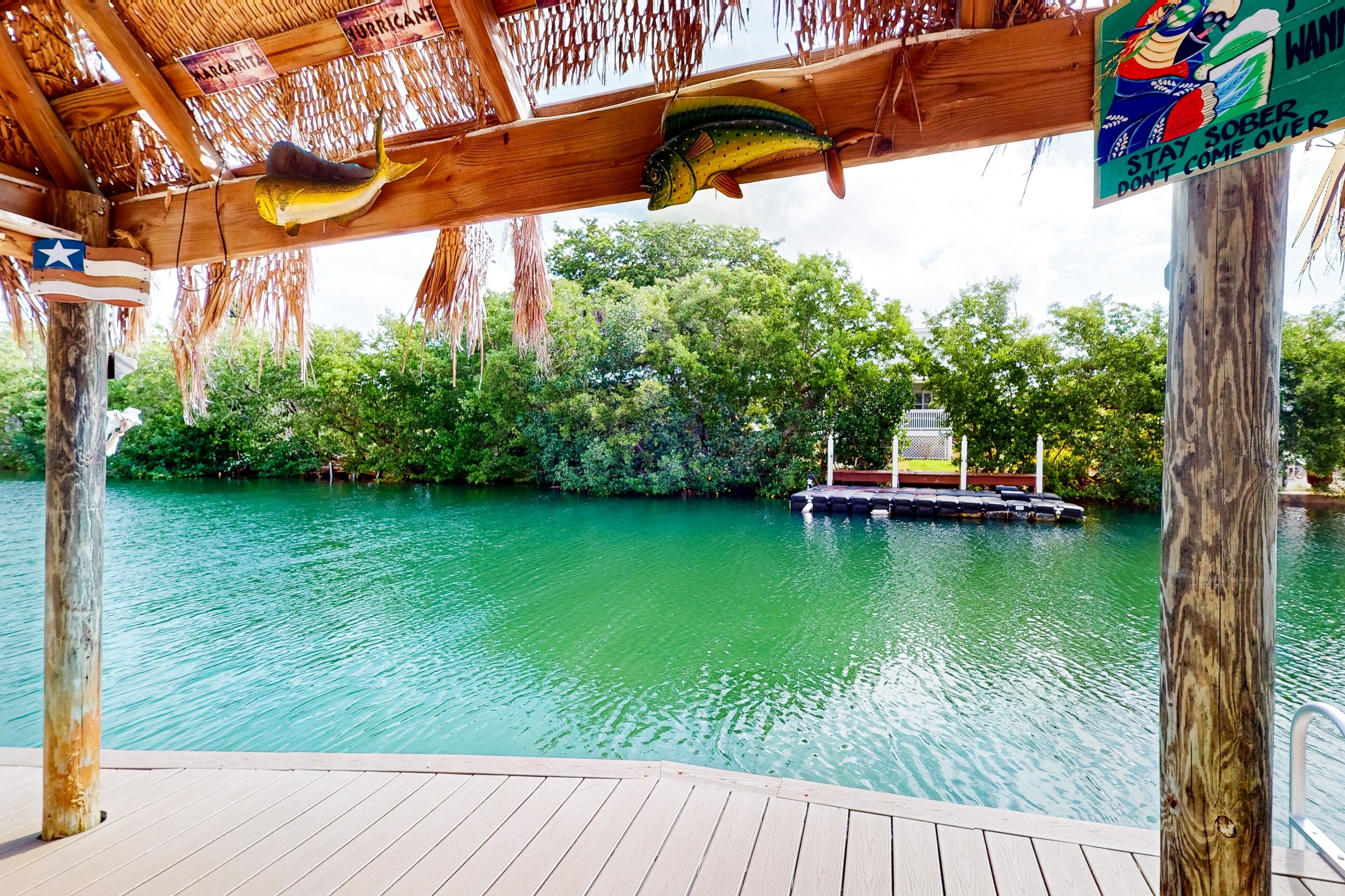 A wooden deck overlooking a calm river with a dock and a boat.