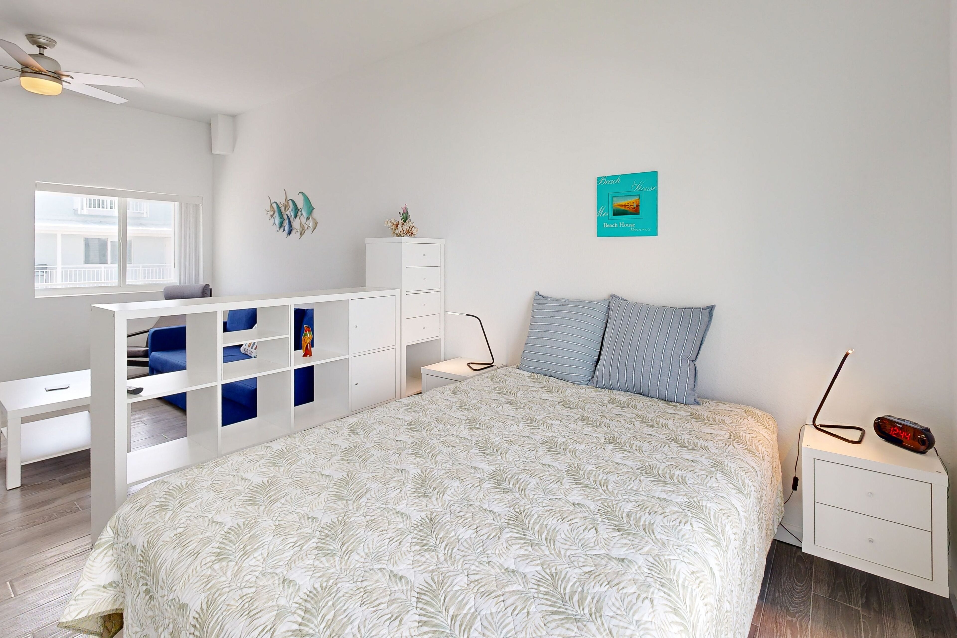 A bedroom with a bed, a white nightstand, a white dresser, a desk, and a window.