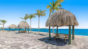 A beachside area with thatched umbrellas, wooden benches, and palm trees. - Gulfside condo with gorgeous views, shared pool, WiFi, & close to attractions (Marathon)