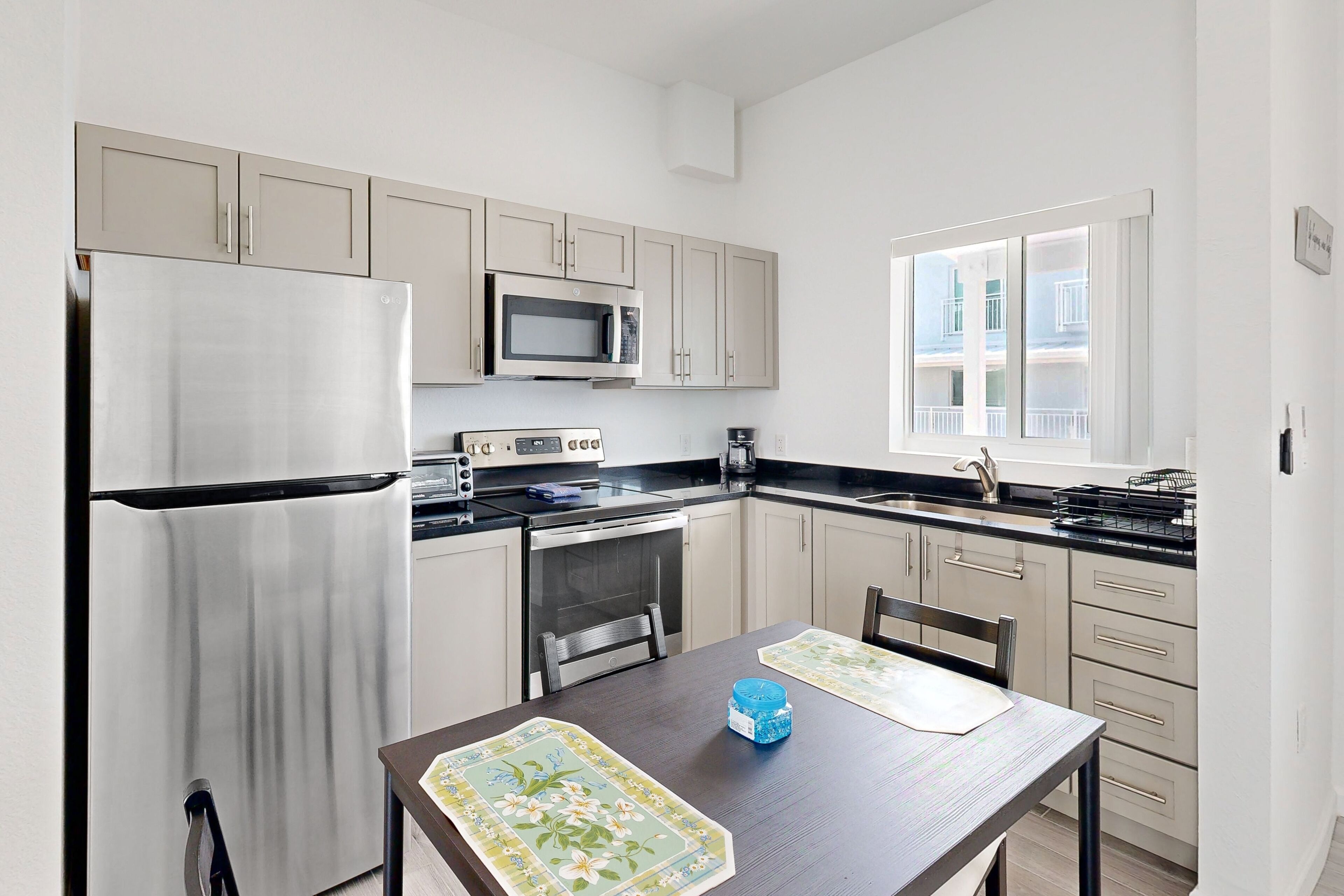 A modern kitchen with stainless steel appliances, a dining table with placemats, and a window with a view of buildings.