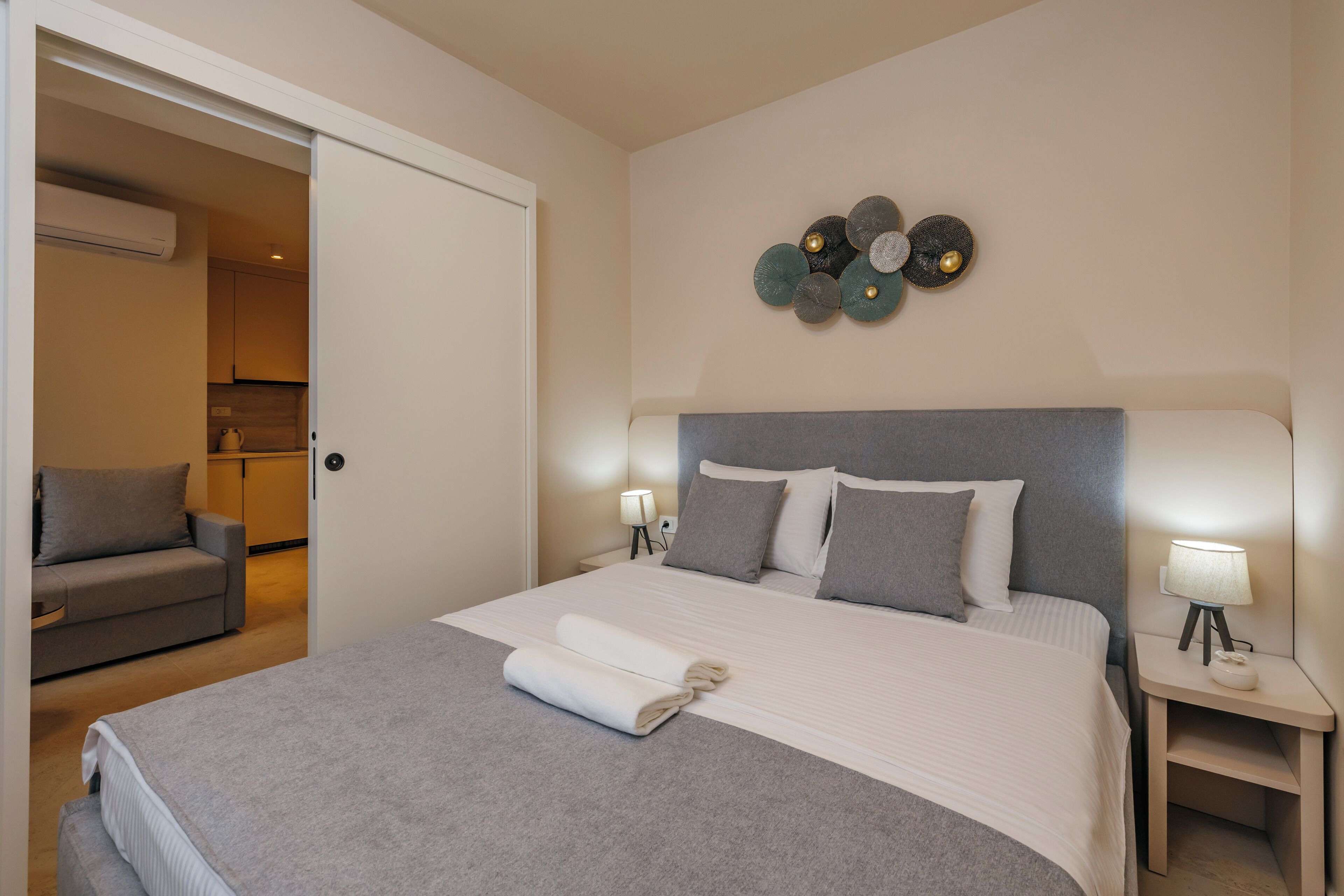 Ein ordentlich bezogenes Bett mit grauer Decke, grauem Kopfteil und zwei Nachttischlampen.