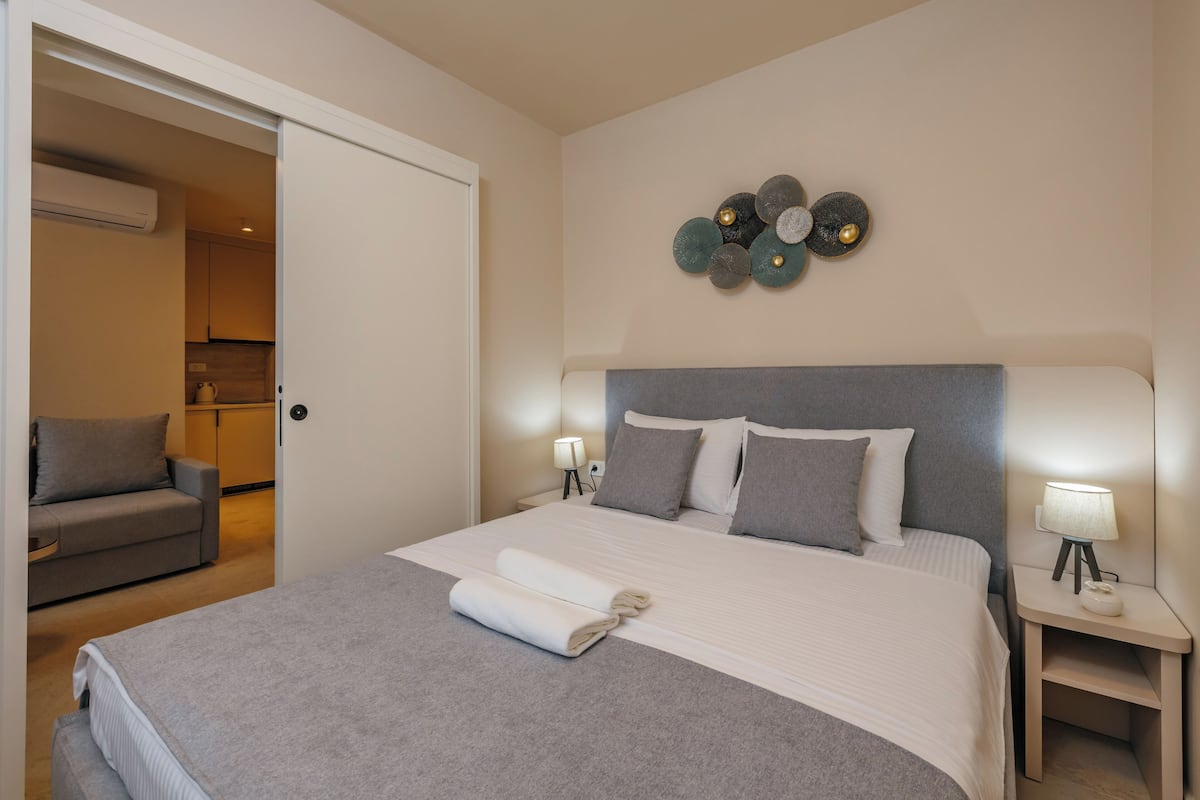 Ein ordentlich bezogenes Bett mit grauer Decke, grauem Kopfteil und zwei Nachttischlampen.