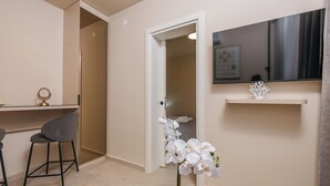 Une chambre d’hôtel équipée d’un bureau, d’une chaise, d’un téléviseur fixé au mur et d’une orchidée en pot posée sur le sol.