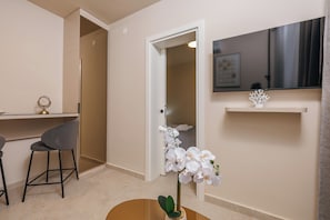 Une chambre dâhĂŽtel Ă©quipĂ©e dâun bureau, dâune chaise, dâun tĂ©lĂ©viseur fixĂ© au mur et dâune orchidĂ©e en pot posĂ©e sur le sol.