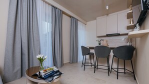 Une cuisine moderne avec des rideaux gris, un coin repas avec trois chaises et une petite table sur laquelle on trouve des magazines et un vase de fleurs.