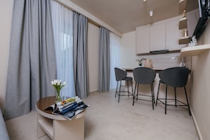 Eine moderne Küche mit grauen Vorhängen, ein Essbereich mit drei Stühlen und einem kleinen Tisch mit Zeitschriften und einem Blumenstrauß.