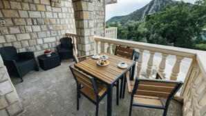 Une terrasse extérieure avec des murs en pierre, une table en bois et des chaises, offrant une vue sur un paysage montagneux.