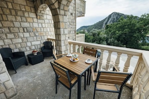 Une terrasse extérieure avec des murs en pierre, une table en bois et des chaises, offrant une vue sur un paysage montagneux.