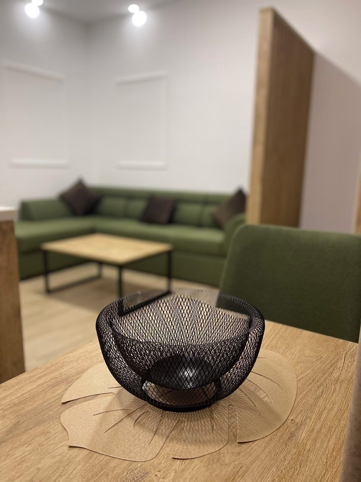 Un intérieur moderne avec une table en bois, une chaise noire en résille, un canapé vert et une cloison en bois.