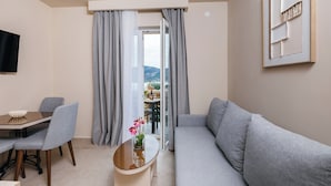 Un salon moderne comprenant un canapé, une table à manger avec des chaises, une table basse avec un vase et un téléviseur fixé au mur.