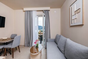 Ein modernes Wohnzimmer mit einer Couch, einem Esstisch mit Stühlen, einem Couchtisch mit einer Vase und einem an der Wand montierten Fernseher.
