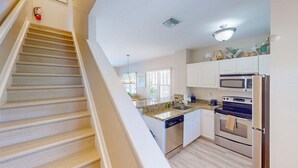A kitchen with a wooden staircase, white cabinets, a dishwasher, a microwave, and an oven. - Enchanting waterfront townhouse with balcony, mini oasis pool, & washer/dryer (Duck Key)