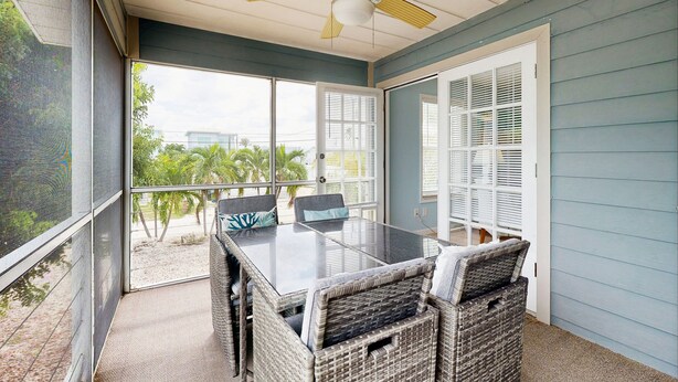 A covered patio with a glass-top table and wicker chairs, overlooking a garden with palm trees. - Charming home close to the ocean with pool, outdoor dining area and grill (Marathon)