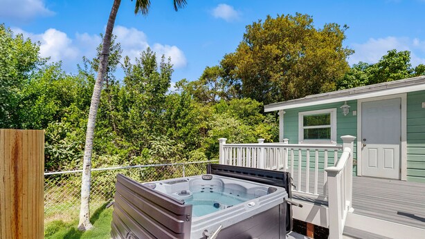 Ein Whirlpool auf einer Holterrasse mit weißer Reling, umgeben von üppiger Vegetation und einem kleinen Gebäude mit grüner Tür.