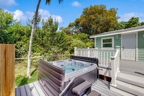 A hot tub on a wooden deck with a white railing, surrounded by lush greenery and a small building with a green door. - Lovely dog-friendly home near the ocean with hot tub & grill (Big Pine Key)
