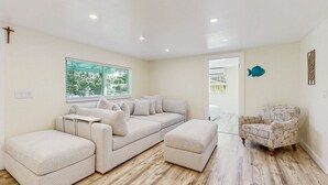 Ein modernes Wohnzimmer mit Ecksofa, Ottoman und einem gemusterten Sessel.