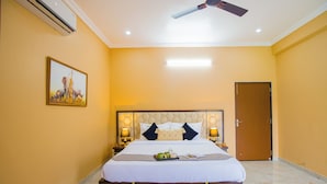 A hotel room with a bed, bedside lamps, a ceiling fan, a door, and a wall-mounted air conditioner. - ELIVAAS The Bliss Hushwood 2 BHK Villa  (Mavli)