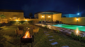 A backyard with a swimming pool, a fire pit, outdoor furniture, and a covered seating area. - ELIVAAS The Bliss Hushwood 2 BHK Villa  (Mavli)