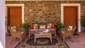 A room with a stone wall, two wooden doors, a sofa, two wicker chairs, a coffee table, and potted plants. - ELIVAAS The Bliss Hushwood 2 BHK Villa  (Mavli)