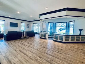 A spacious living area with a black sofa, wooden flooring, and large windows.