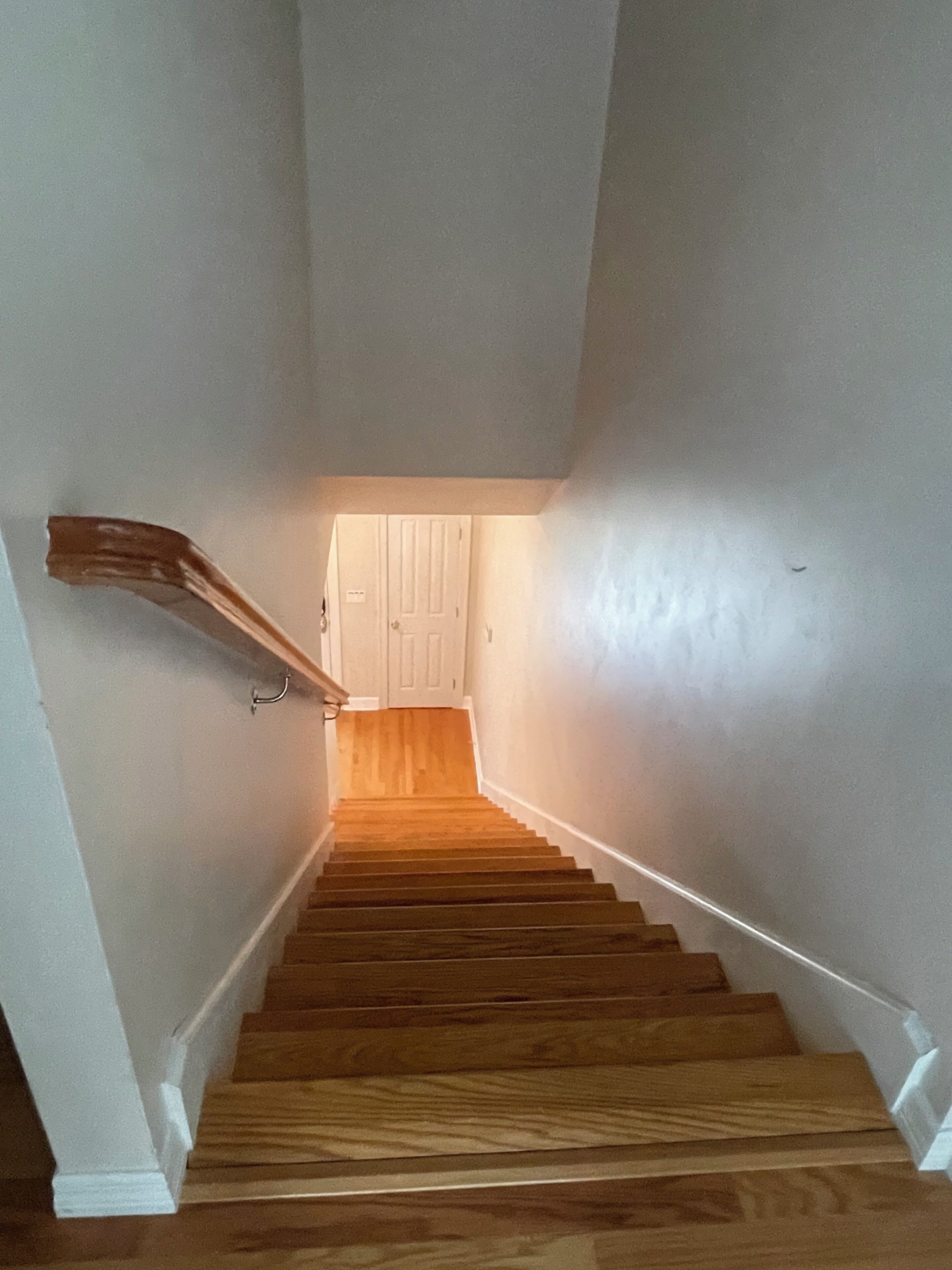 A wooden staircase with white walls and a door at the top.