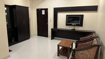 A hotel room with a TV, a sofa, a small table, and a wardrobe.