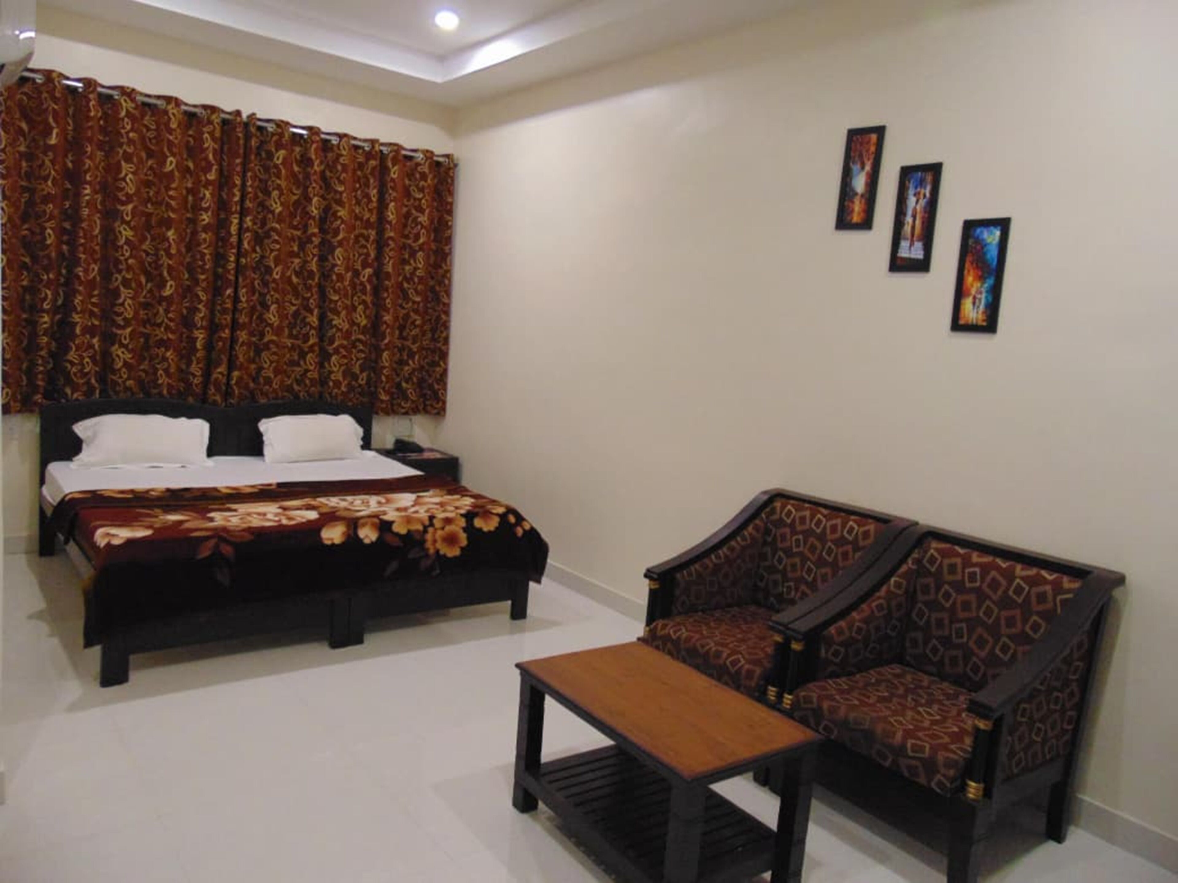 A hotel room with a bed, a sofa, a small table, and three framed pictures on the wall.