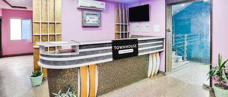 A reception desk with a sign reading 'TOWNHOUSE,' air conditioning units, a mounted television, and a staircase leading to an upper level.