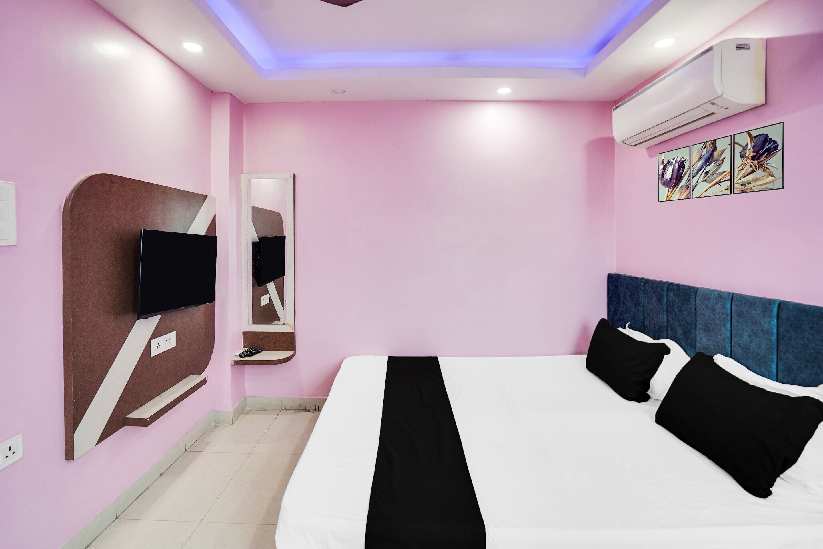 A pink-walled hotel room with a bed, a flat-screen TV, a mirror, and an air conditioner.