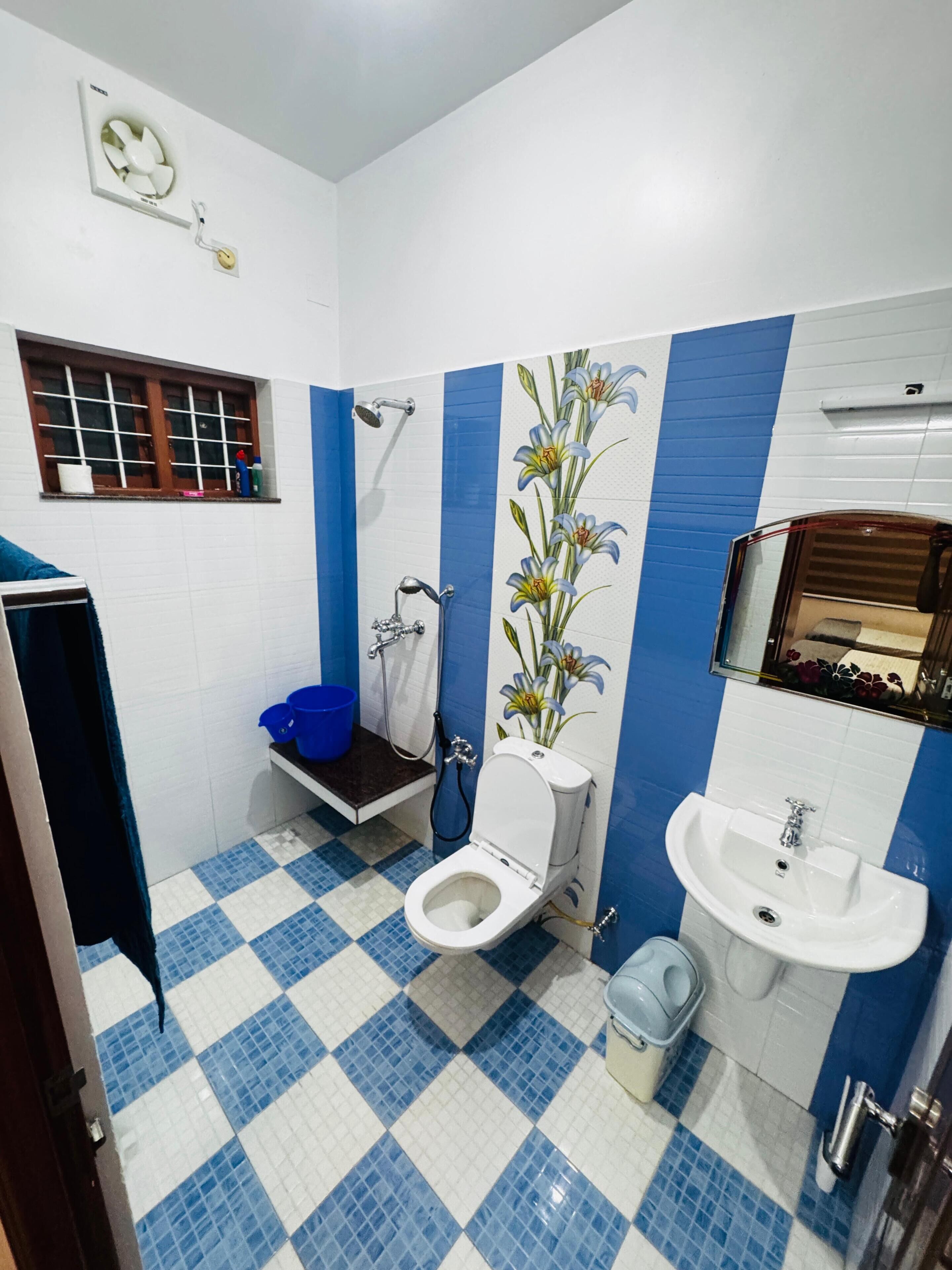 Et badeværelse med toilet, vask, bruser og et vindue med udsigt.